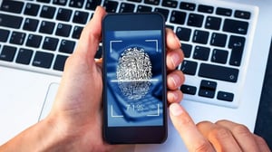 User scanning fingerprint on smartphone for security access, with laptop in background.
