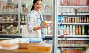 Smiling girl holding a juice bottle in an automated store with refrigerated drink displays.