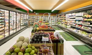 Grocery store produce aisle with fresh fruits, vegetables, and refrigerated shelves.