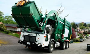 Garbage truck collecting waste bins in a residential neighborhood.